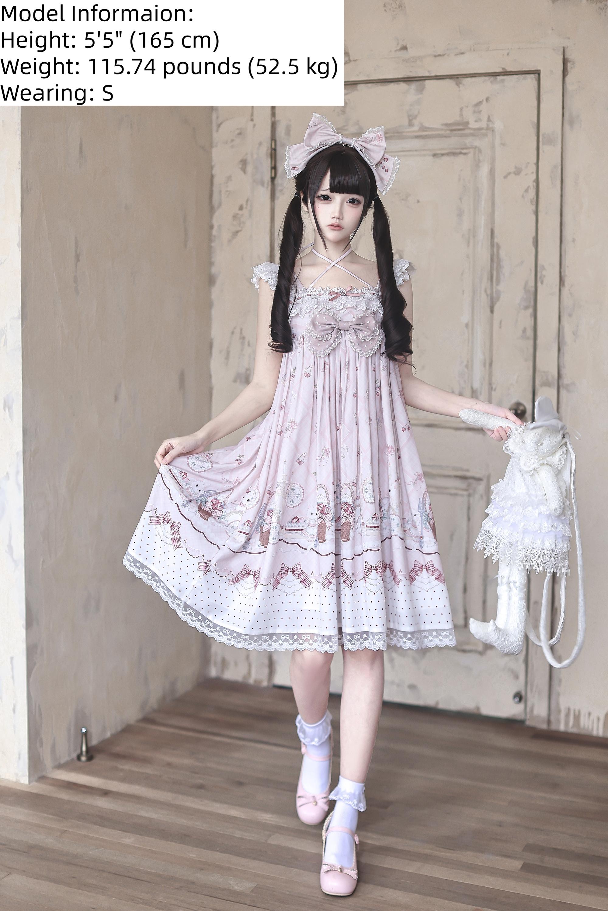 Three-quarter front view of strawberry bunny Jirai Kei Lolita dress showing ruffled straps lace rabbit bag accessory lace hem and model with matching hair bow in vintage interior