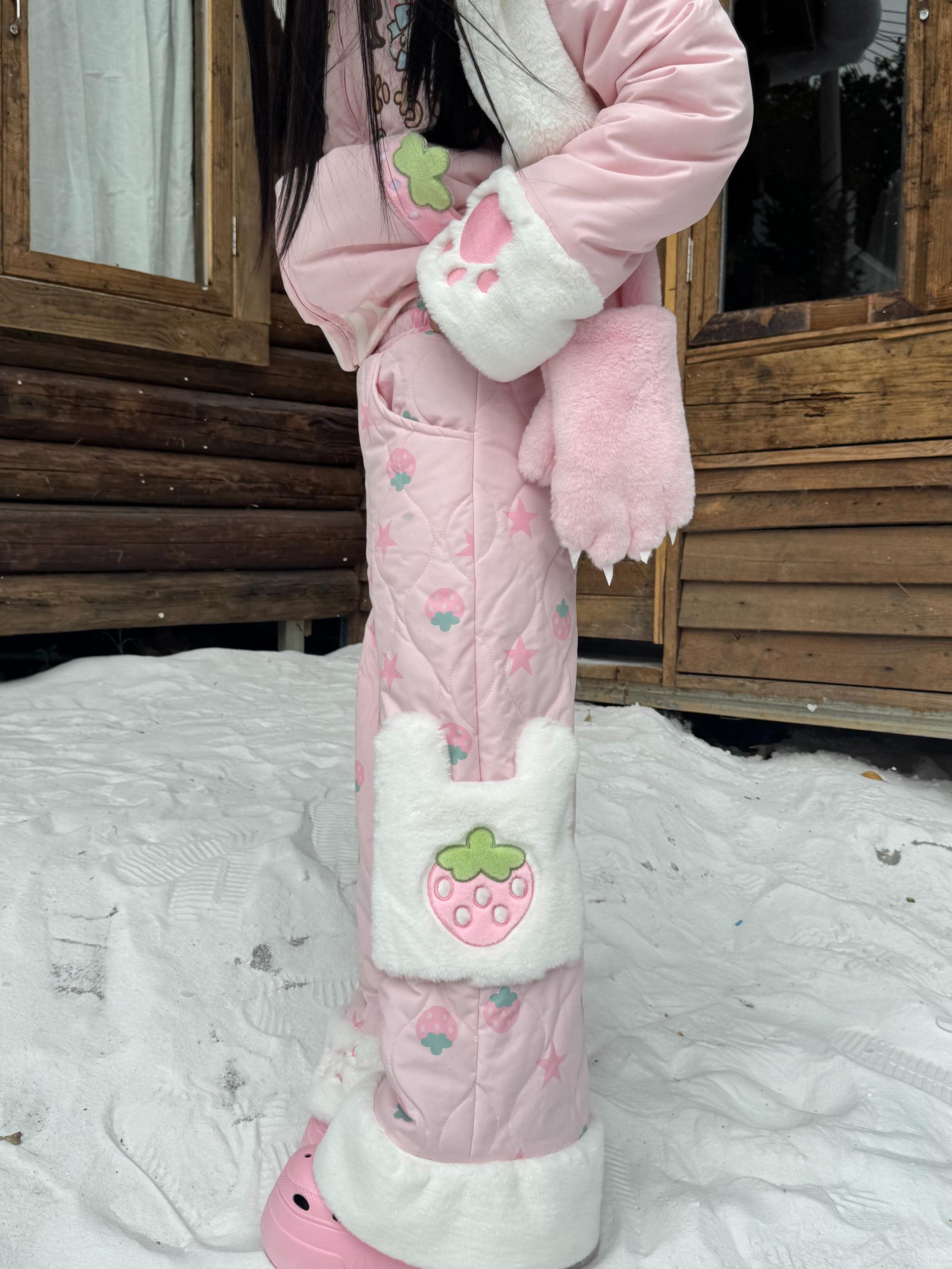 Strawberry Jirai Kei quilted pink cotton pants close-up front view showing fuzzy white trims and strawberry print detail with side pocket patch in snowy cabin setting