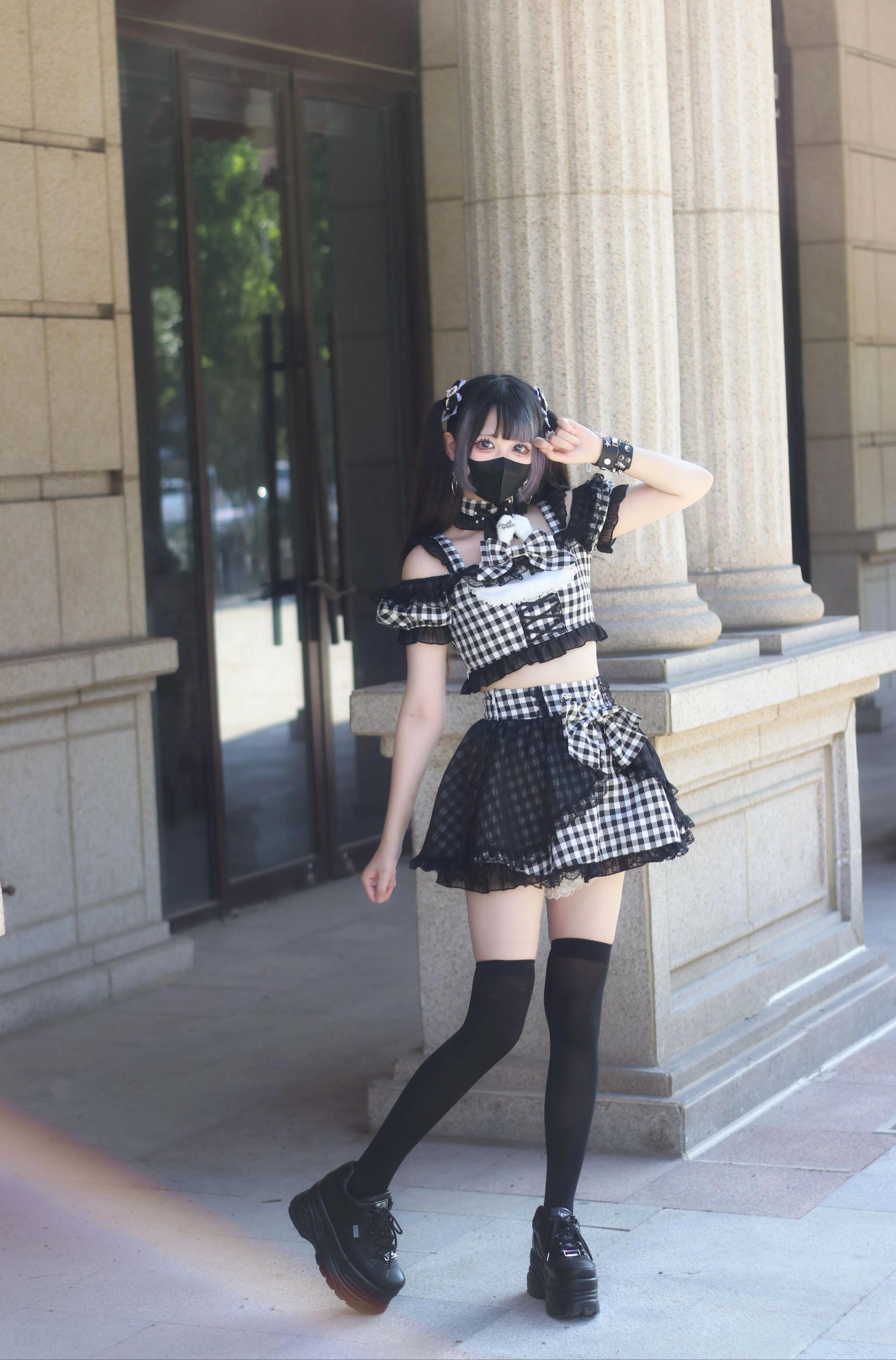 Black cat ear jirai kei maid lolita outfit full body side view outdoor building entrance with cropped top short skirt and thigh-high socks
