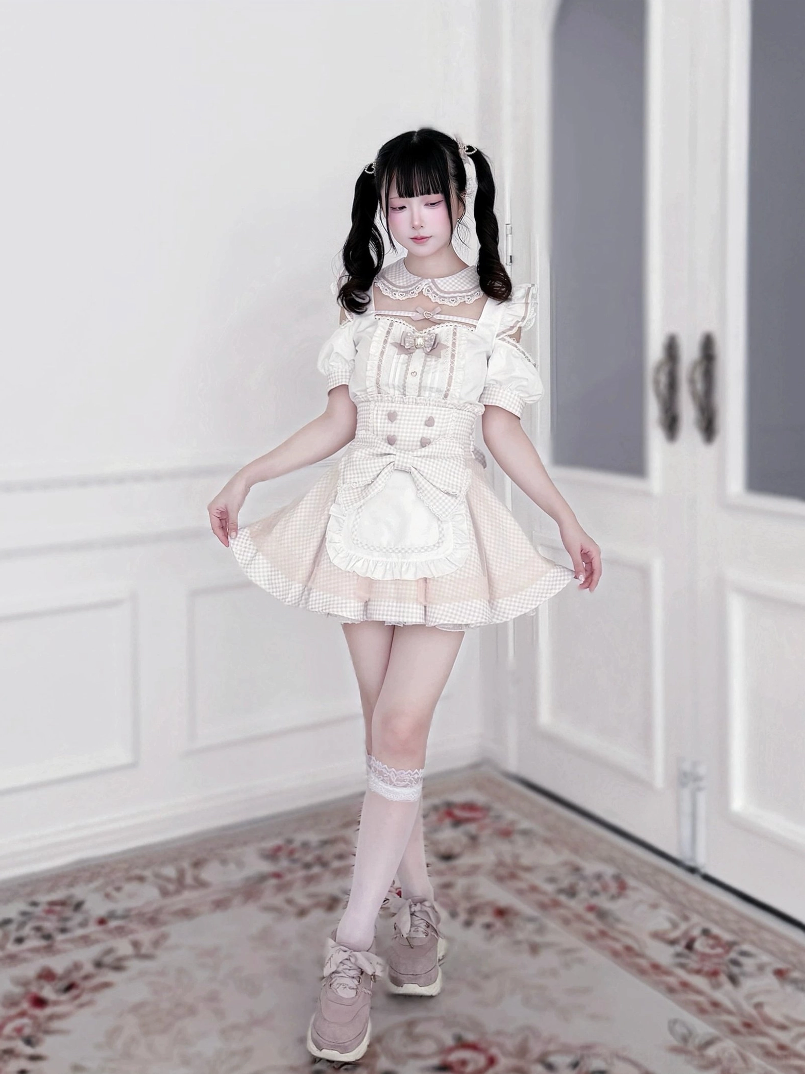 Full body front view of pink and white gingham Jirai Kei maid outfit set with ruffled detachable apron, Peter Pan collar, and heart button accents worn indoors