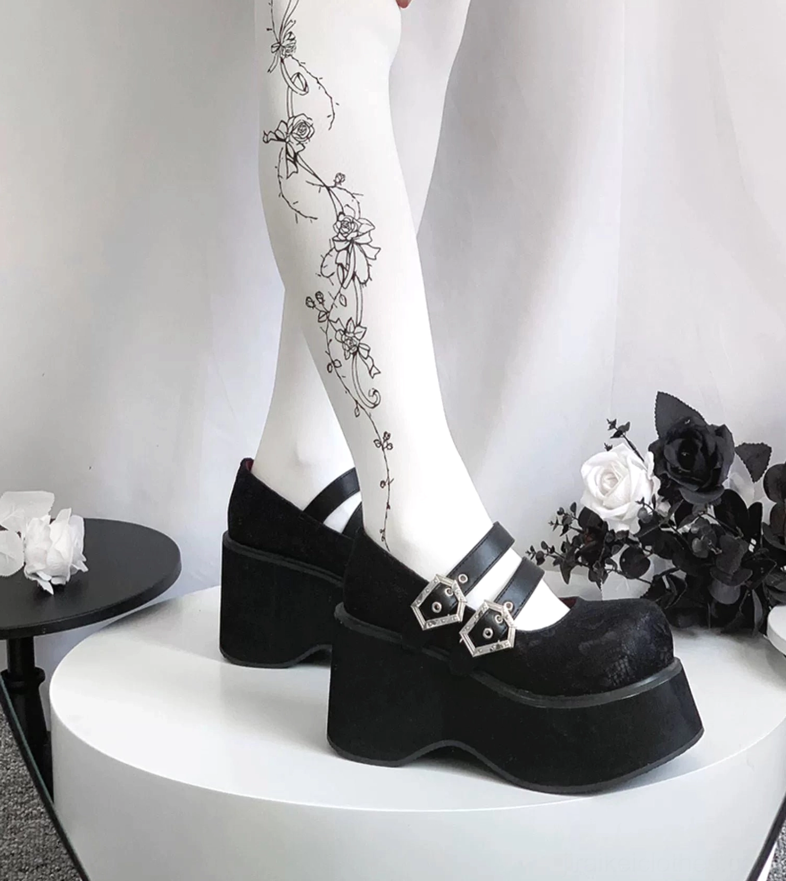 Matte black leather Mary Jane platform shoes on model legs wearing floral tattoo tights showing suede-style thick platform sole and decorative silver buckles
