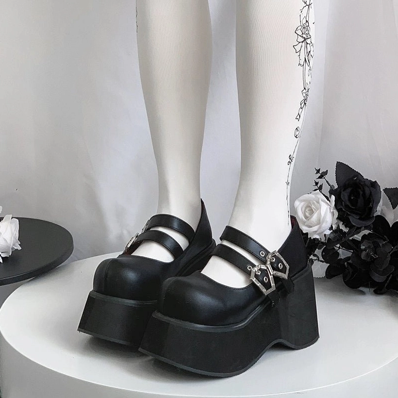 Solid black leather Mary Jane platform shoes on model legs with dual silver buckles thick wedge sole low angle front view on white display stand gothic decor