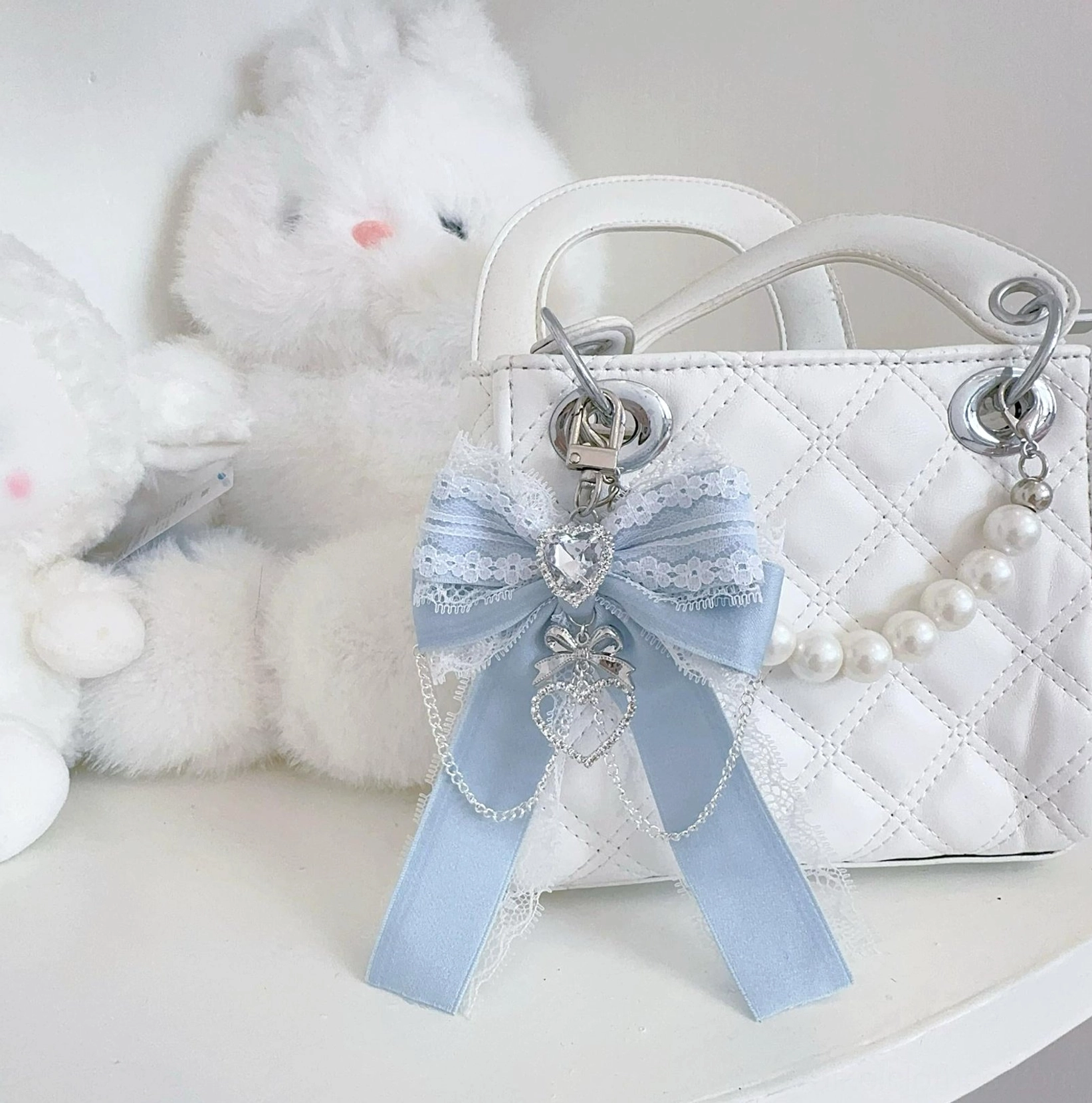Gray-blue Ryousangata bow bag pendant with heart rhinestone on quilted handbag - close-up detail view of pearl chain accent and lace trim for Jirai Kei fashion