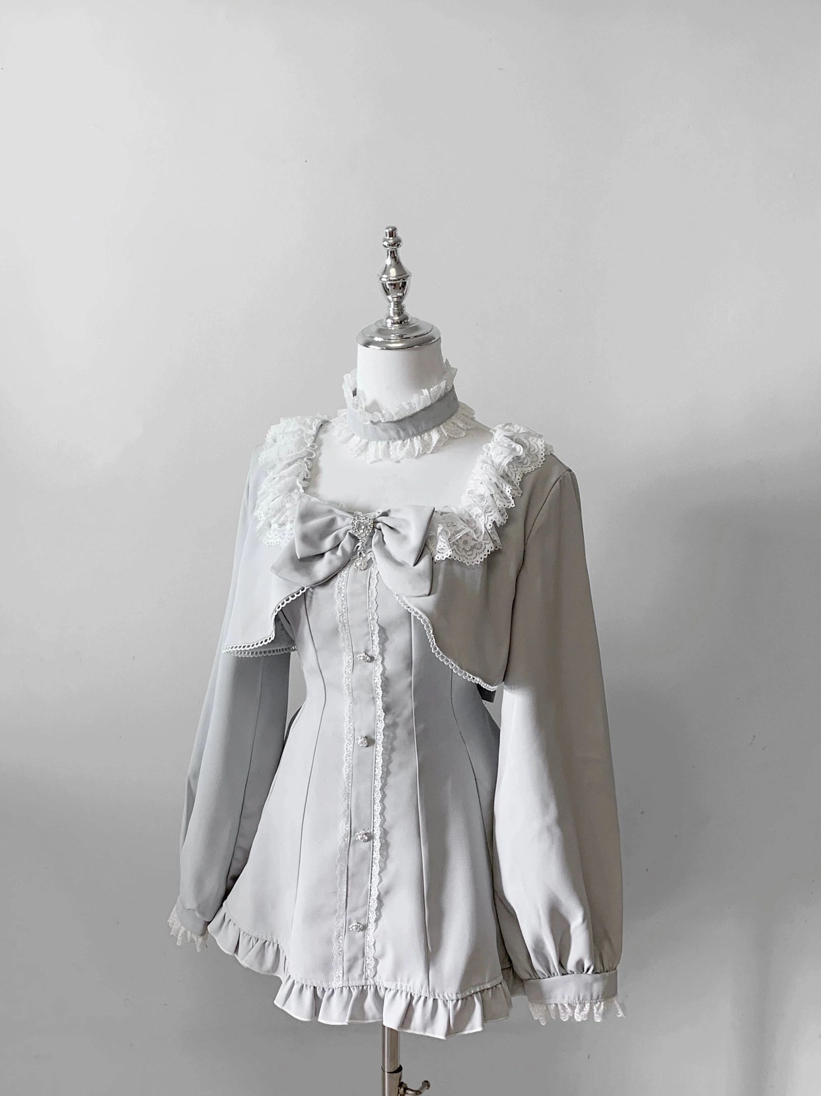 Light gray gothic Jirai Kei dress with contrast sleeves, lace collar, front bow accent, and ruffled hem on mannequin showcase