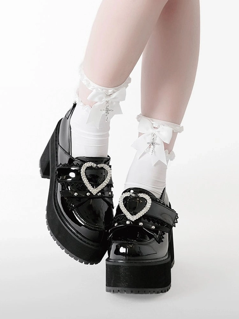 Low-angle side close-up of black glossy patent leather heart buckle platform loafers showing shiny finish, chunky block heel, and rhinestone embellishments with frilled bow white ankle socks