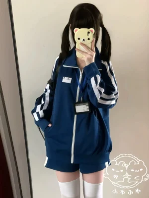 Navy Jersey Maid sports jacket with white sleeve stripes and name label patch worn with white maid apron, mirror selfie of twin-tail model in casual home interior, work-style aesthetic