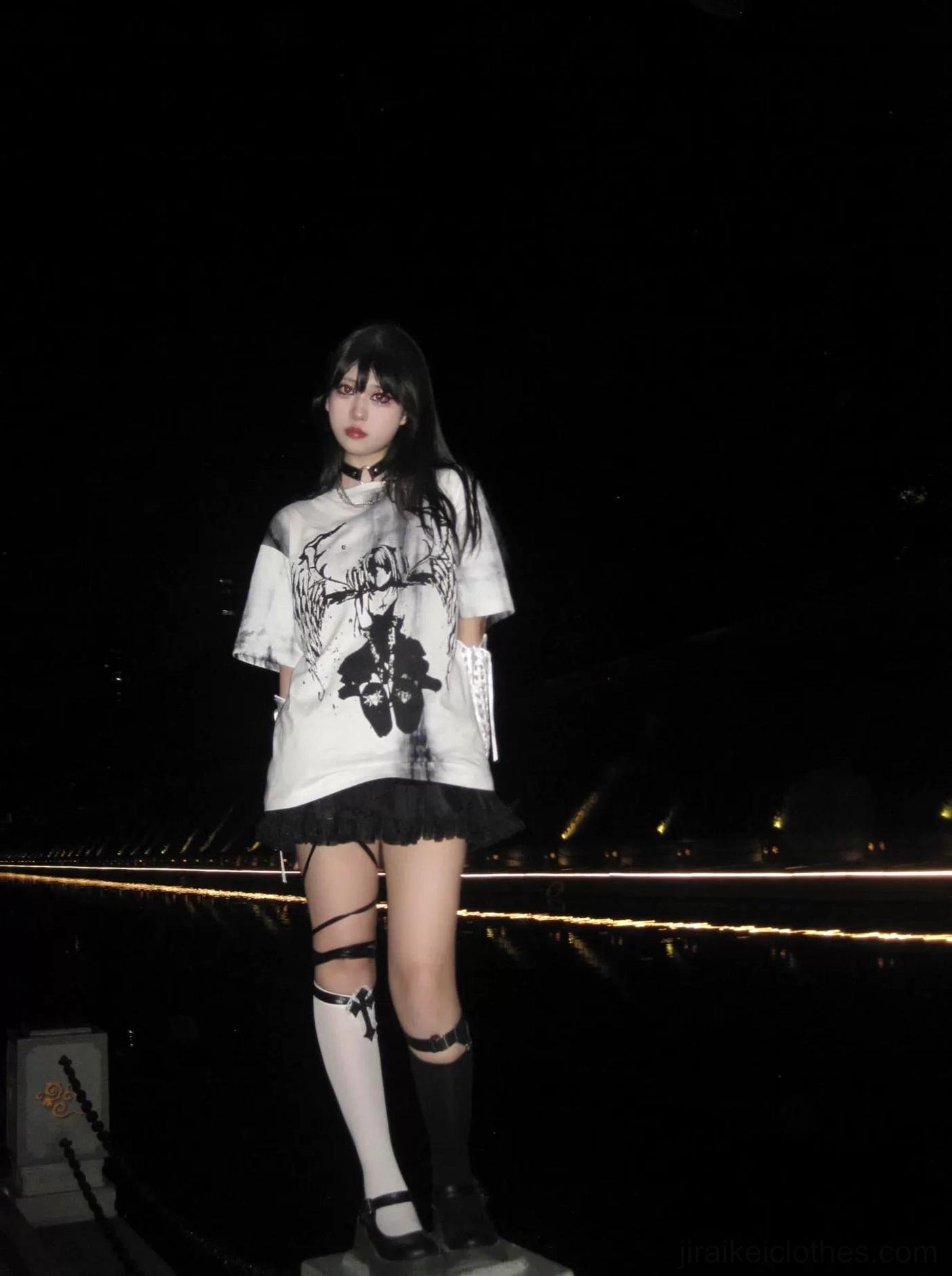 Black-haired model wearing oversized tie-dye gothic jirai kei angel wings t-shirt paired with ruffled black skirt, night riverside full-body look