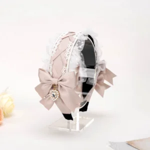 Three-quarter side view of ashy-pink Jirai Kei hairband with crossed lace trim, double satin bows, and heart diamond pendant displayed on clear acrylic stand