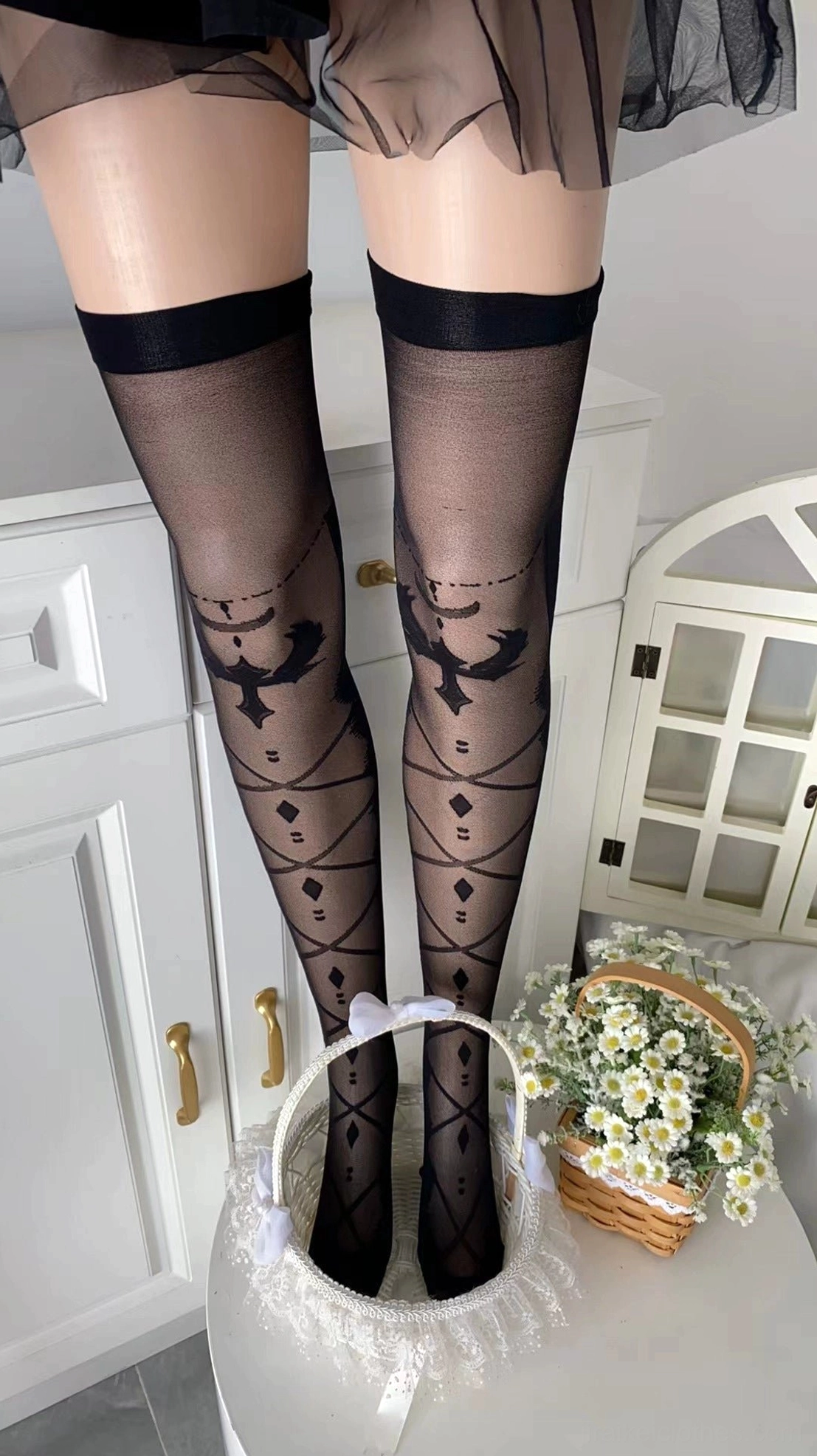 Black with bow Jirai Kei over-the-knee printed velvet socks featuring bat and geometric hollow patterns with solid lace top, front low-angle view in home kitchen setting, bold statement piece showcasing darker aesthetic