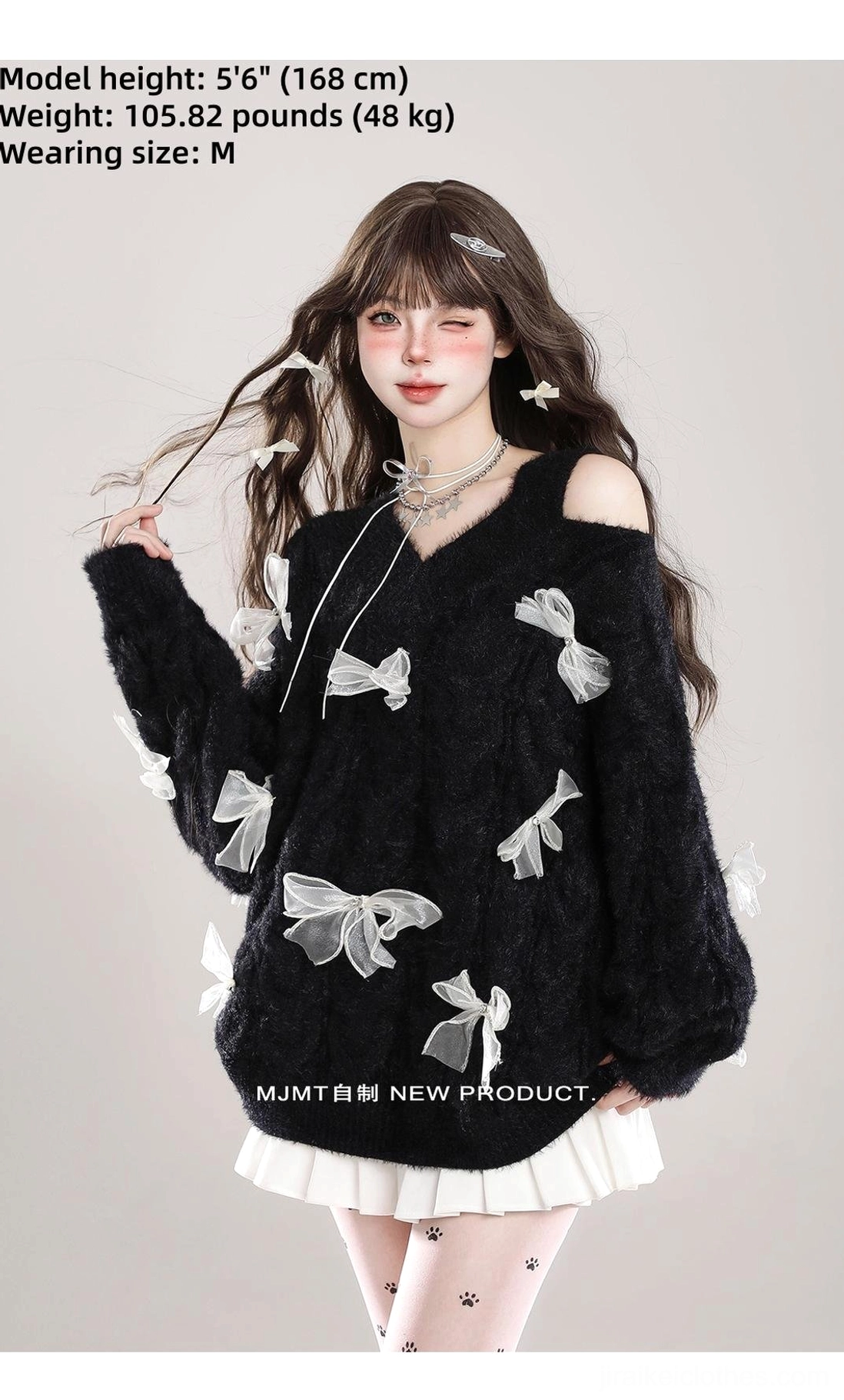 Black Jirai Kei cold-shoulder fuzzy bow sweater with size chart information, white ribbon bows, V-neck asymmetrical cut, modeled with pleated skirt and printed tights, full-body front view