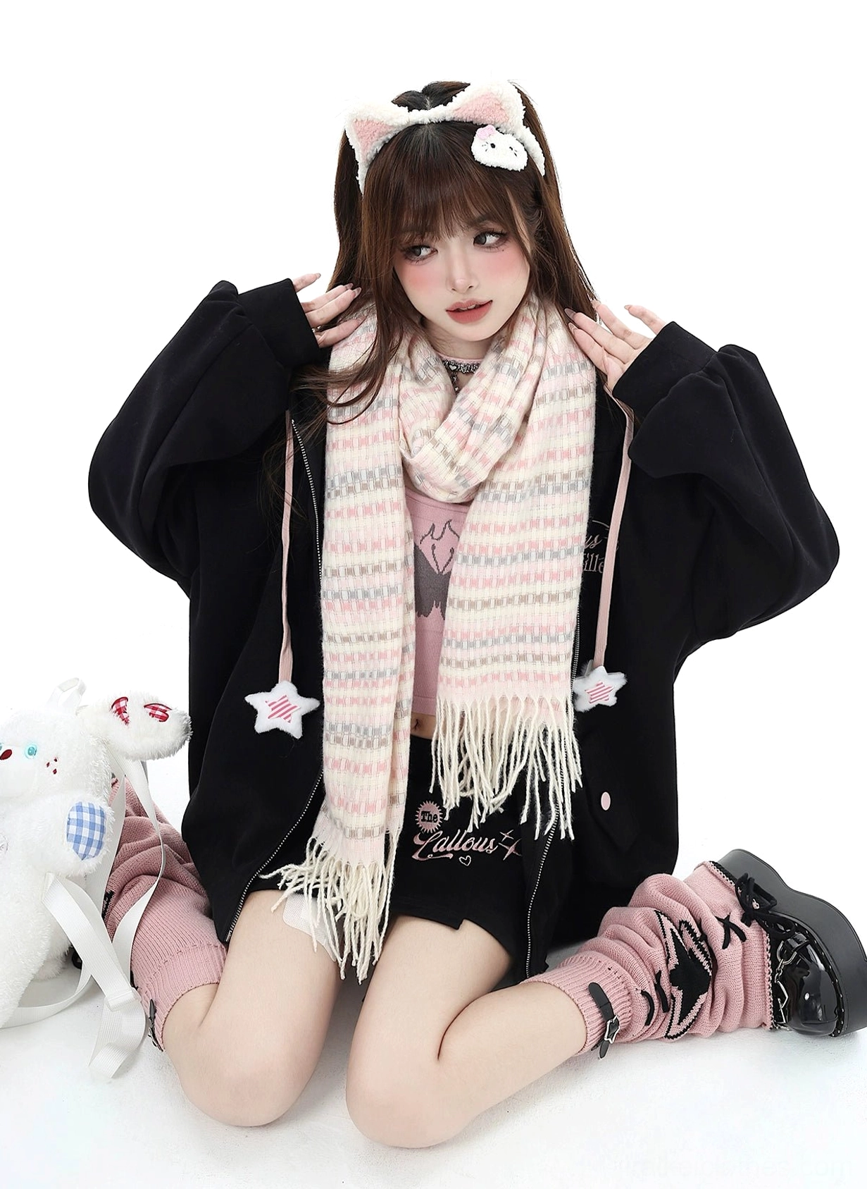 Black Jirai Kei hoodie outfit with pink-white plaid tassel scarf and plush doll accessory, seated front view on studio background