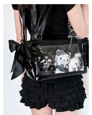 Black glossy Jirai Kei ita crossbody bag worn by model in Lolita dress, displaying plush anime dolls in transparent window with side ribbon bows
