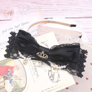 Black lace bow headband Jirai Kei style with ornamental crown charm and pearl gem pendant dangles, top-down view on vintage wooden desktop