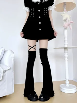 Black jirai kei over-the-knee leg warmers with adjustable cross straps worn with black lolita mini dress, featuring flared hem and thigh straps in indoor home setting