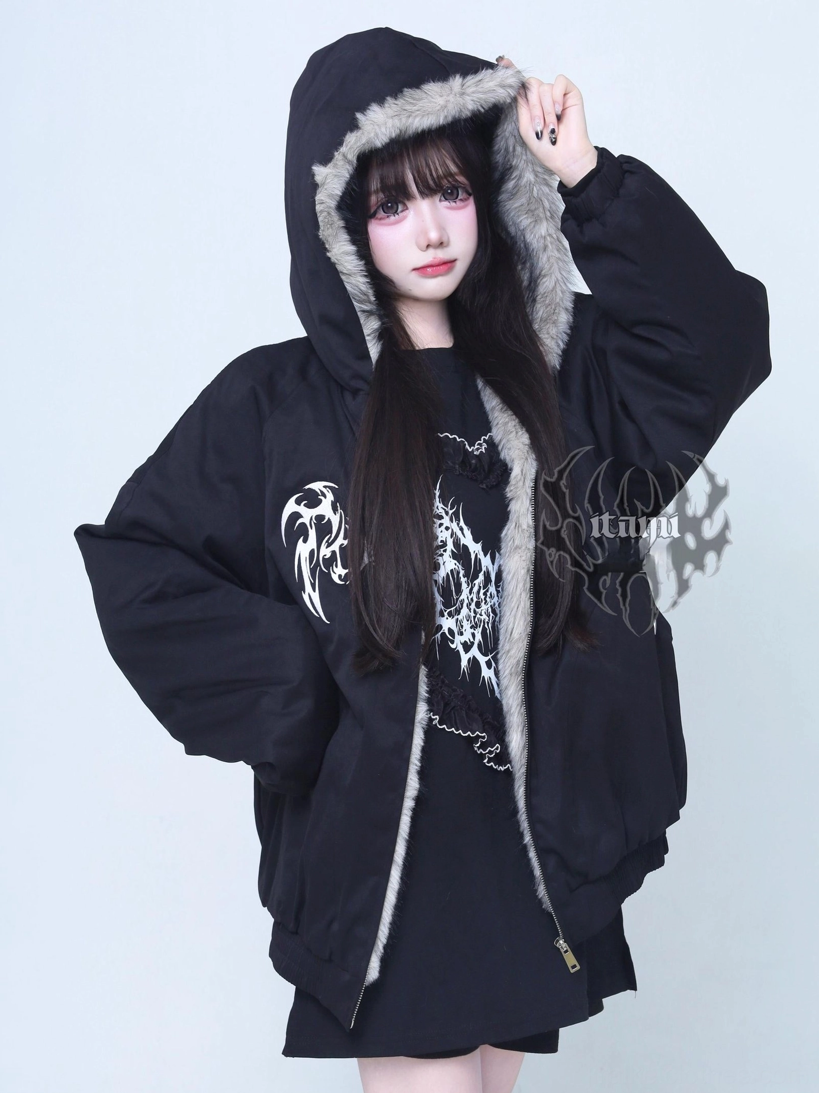 Jirai Kei black padded hooded jacket with white tribal chest embroidery front three-quarter view on female model with grey fur trim hood