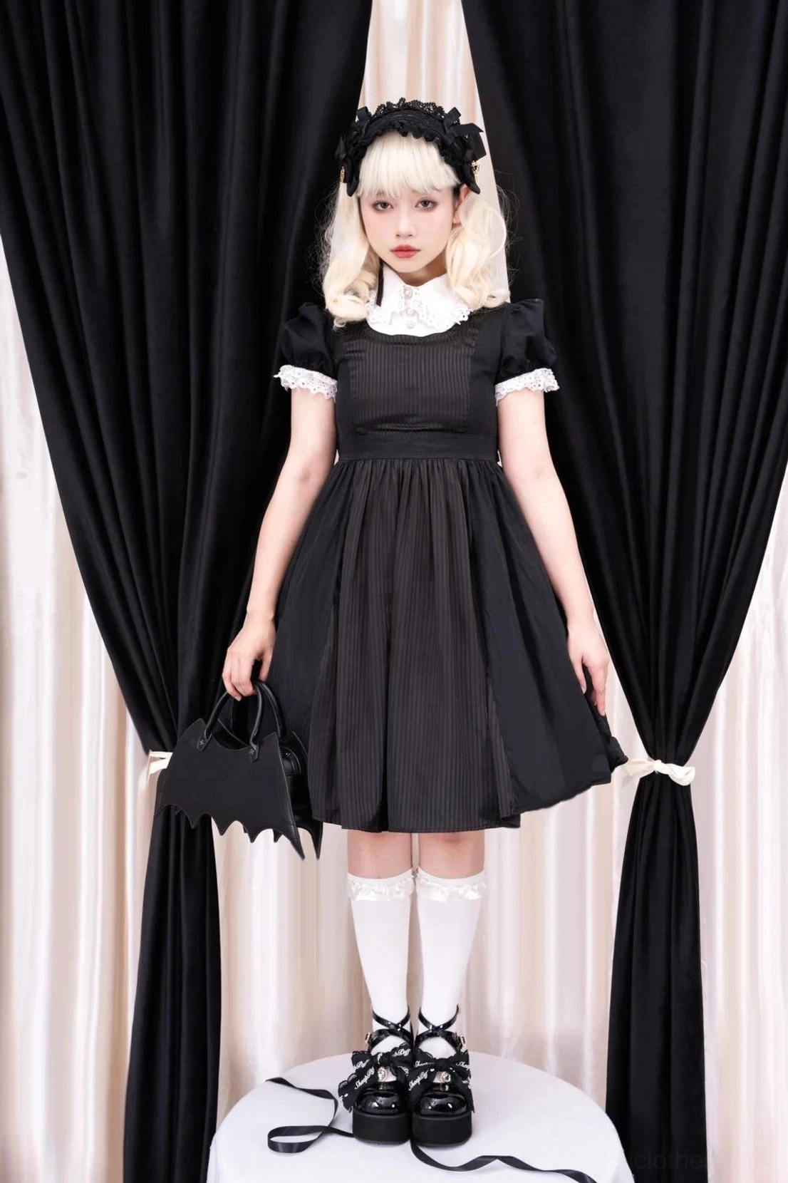 Black patent leather platform Mary Jane Jirai Kei shoes with crisscross buckle straps and bow decorations, worn by gothic lolita model in black dress