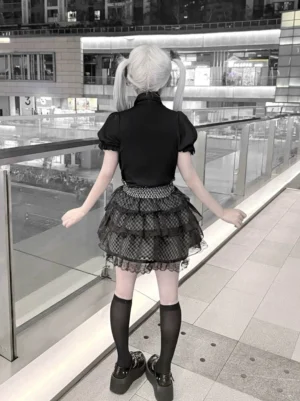 Jirai Kei black blouse plaid skirt back view model wearing short-sleeve black top layered ruffled plaid skirt outdoor mall setting