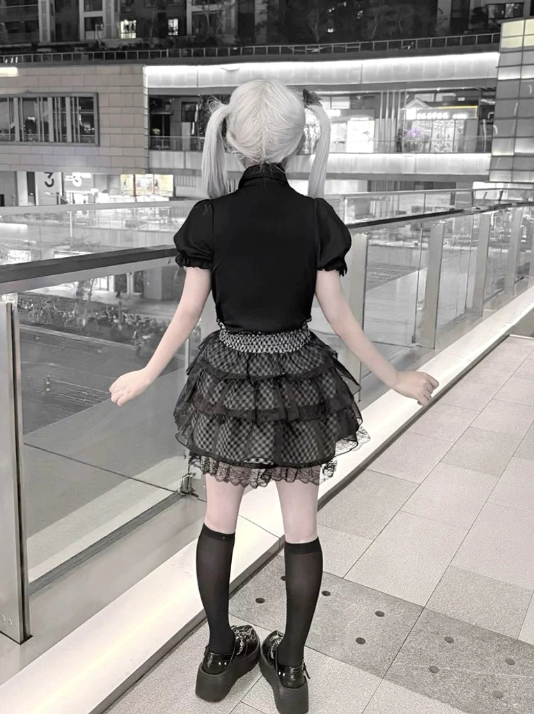 Jirai Kei black blouse plaid skirt back view model wearing short-sleeve black top layered ruffled plaid skirt outdoor mall setting