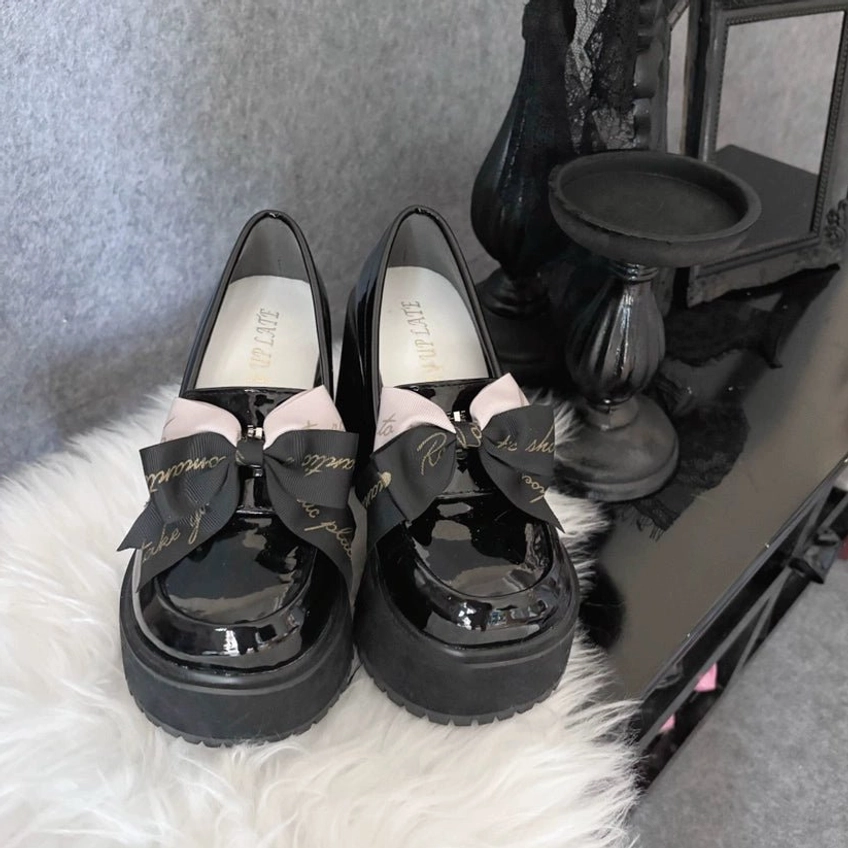 Black Jirai Kei platform heels with glossy patent leather finish and detachable bow decoration, front overhead view showcasing dual-tone bow accent and thick platform sole