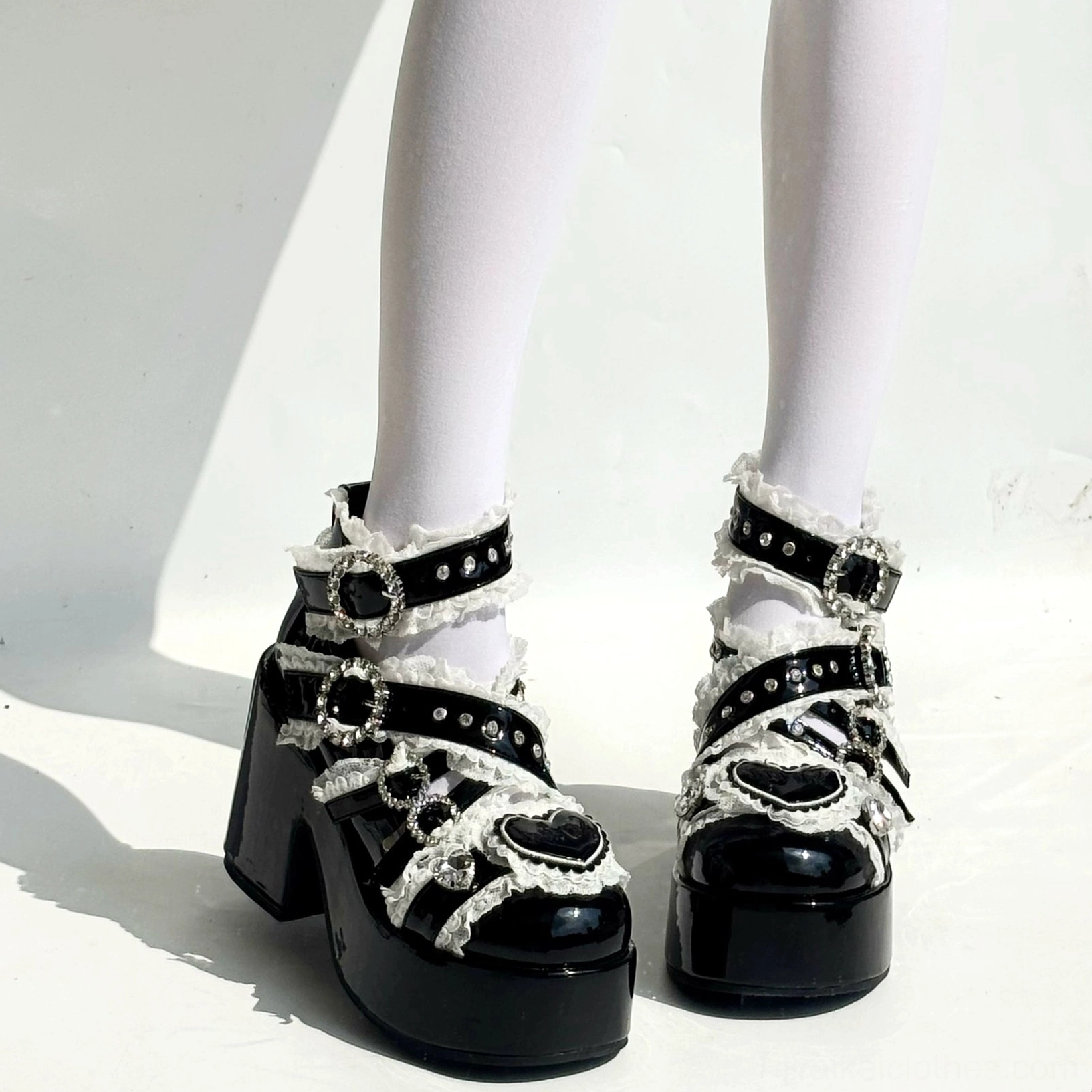 Black Jirai Kei platform heels with ruffled lace trim and heart buckles on model wearing white stockings front view