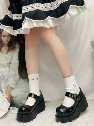 Black glossy patent leather Jirai Kei platform Mary Jane shoes with round toe and ankle strap buckle, worn with black-and-white Lolita skirt and white heart-patterned crew socks on plush carpet with oil painting backdrop