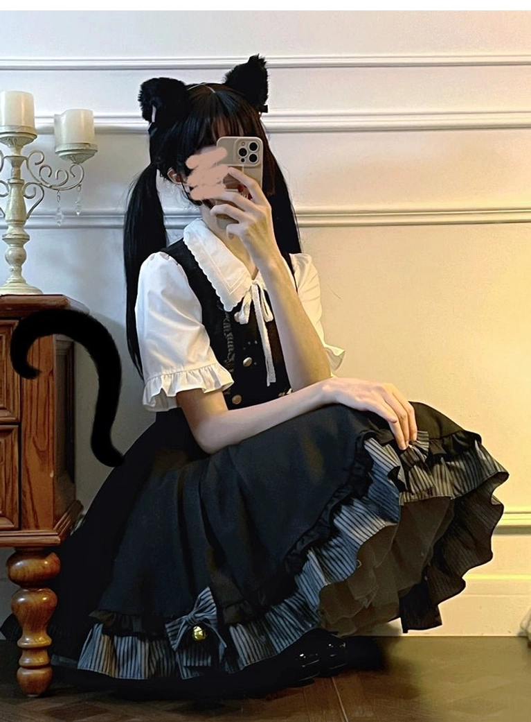 Sitting three-quarter selfie of Jirai Kei preppy ensemble featuring flared ruffled skirt hem with striped trim, bow bell decorations on black suspender skirt, cat ear girl wooden furniture