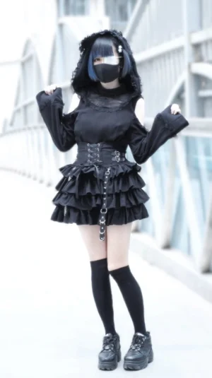 Full body styling of black Jirai Kei outfit with ruffled mini skirt platform loafers and cold-shoulder top outdoor bridge