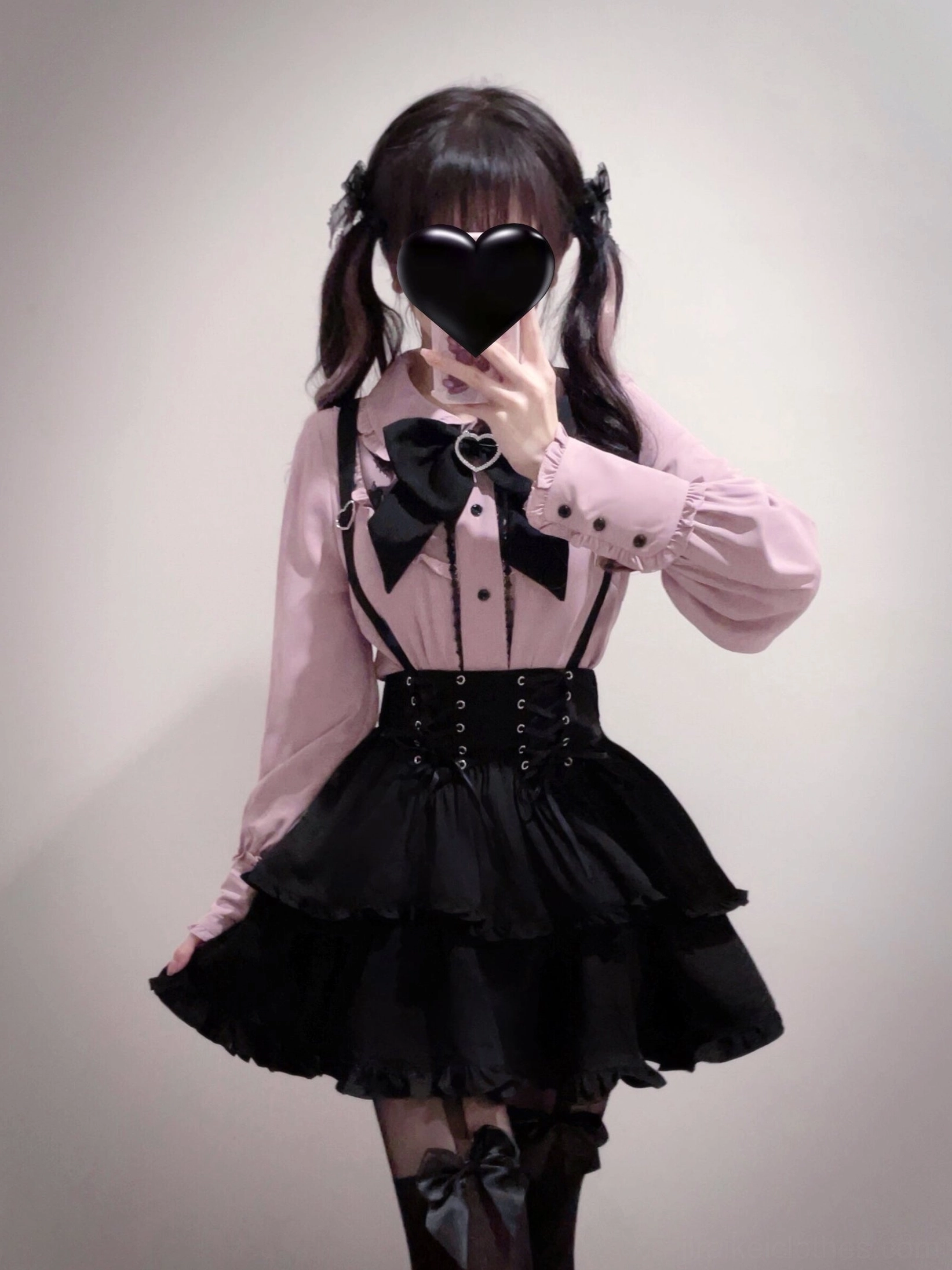Close-up half-body front view of Jirai Kei suspender skirt with black corset waist, ruffled tiered layers, black bow tie detail and pink lacing
