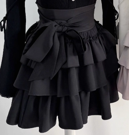 Black tiered ruffle skirt side close-up view matte black fabric detachable waist bow layered ruffle hem construction mannequin
