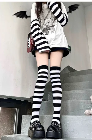Black and white horizontal striped over-the-knee socks worn by female model with arm sleeves, indoor stair setting, Jirai Kei punk aesthetic