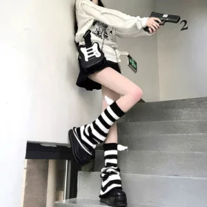 Black and white horizontal striped leg warmers with side wing decorations, side view on model legs in stairwell setting - Jirai Kei punk aesthetic leg warmer