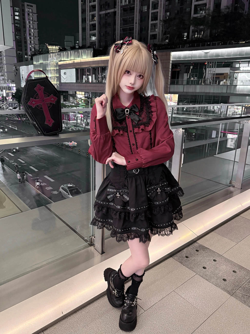 Front three-quarter Jirai Kei fashion look featuring heart-shaped hair clips, lace-trimmed Peter Pan collar on burgundy blouse, and tiered black skirt on nighttime shopping street
