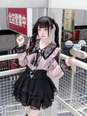 Gothic lolita Jirai Kei blouse pink ruffled style with black lace trim skirt, twin tails model outdoor shop scene, complete outfit view