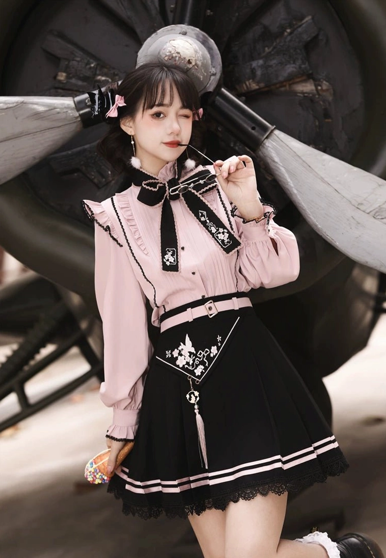 Half-body front shot of Jirai Kei two-piece set featuring decorative bow necktie, heart-shaped buttons, and tassel skirt accessory on model against vintage airplane