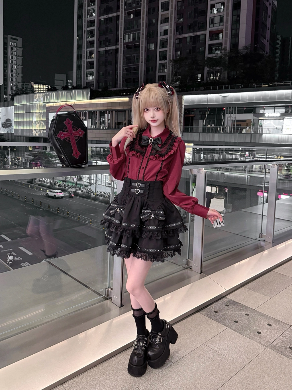 Three-quarter side front perspective of Jirai Kei ensemble with hand resting on decorative collar, showcasing matching wine-and-black outfit on commercial terrace