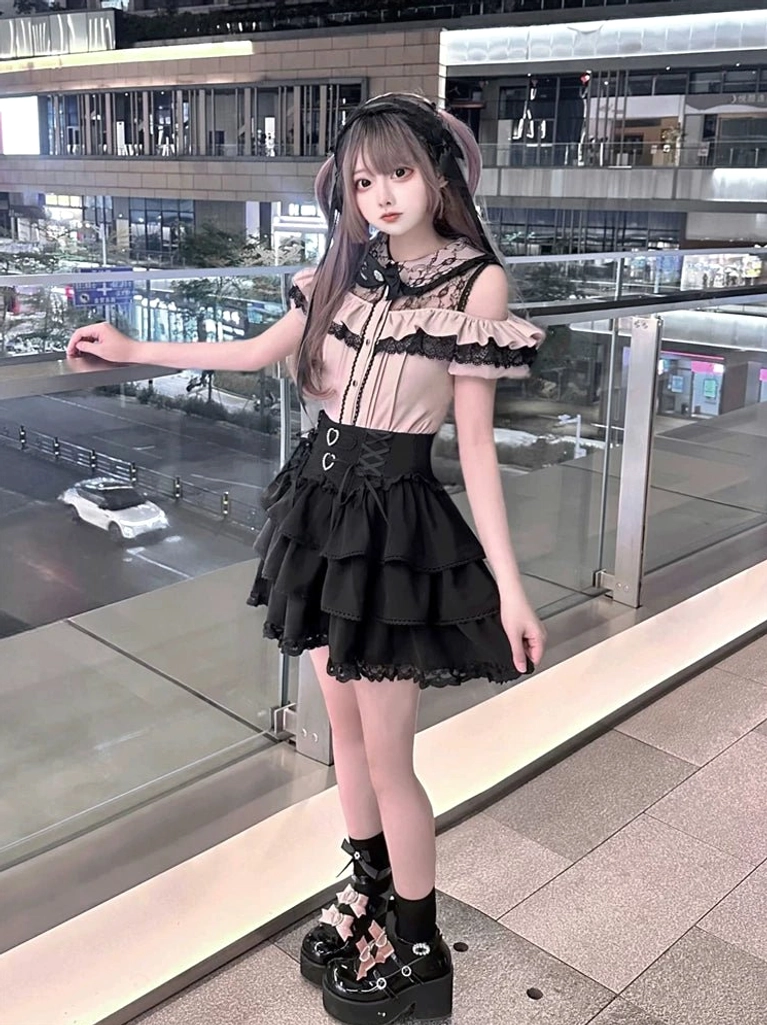 Jirai Kei off-shoulder blouse and tiered skirt oblique angle showing ruffled sleeves, heart-shaped waist buckles, and Gothic lolita aesthetic on young female model at night shopping mall