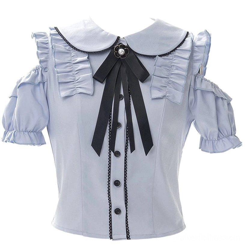 Close-up flat lay of light blue cold-shoulder blouse highlighting delicate flower brooch on black ribbon bow, ruffled shoulder details, and intricate decorative stitch trim