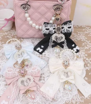 Multiple Jirai Kei bow bag charms with pastel and black lace bows featuring rhinestone and pearl embellishments on pink quilted handbag