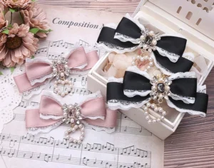 Jirai Kei bow hair clips flat lay display with black-white and pink color variants shown on white plate with sheet music and dried flowers background, featuring rhinestone and pearl pendant embellishments