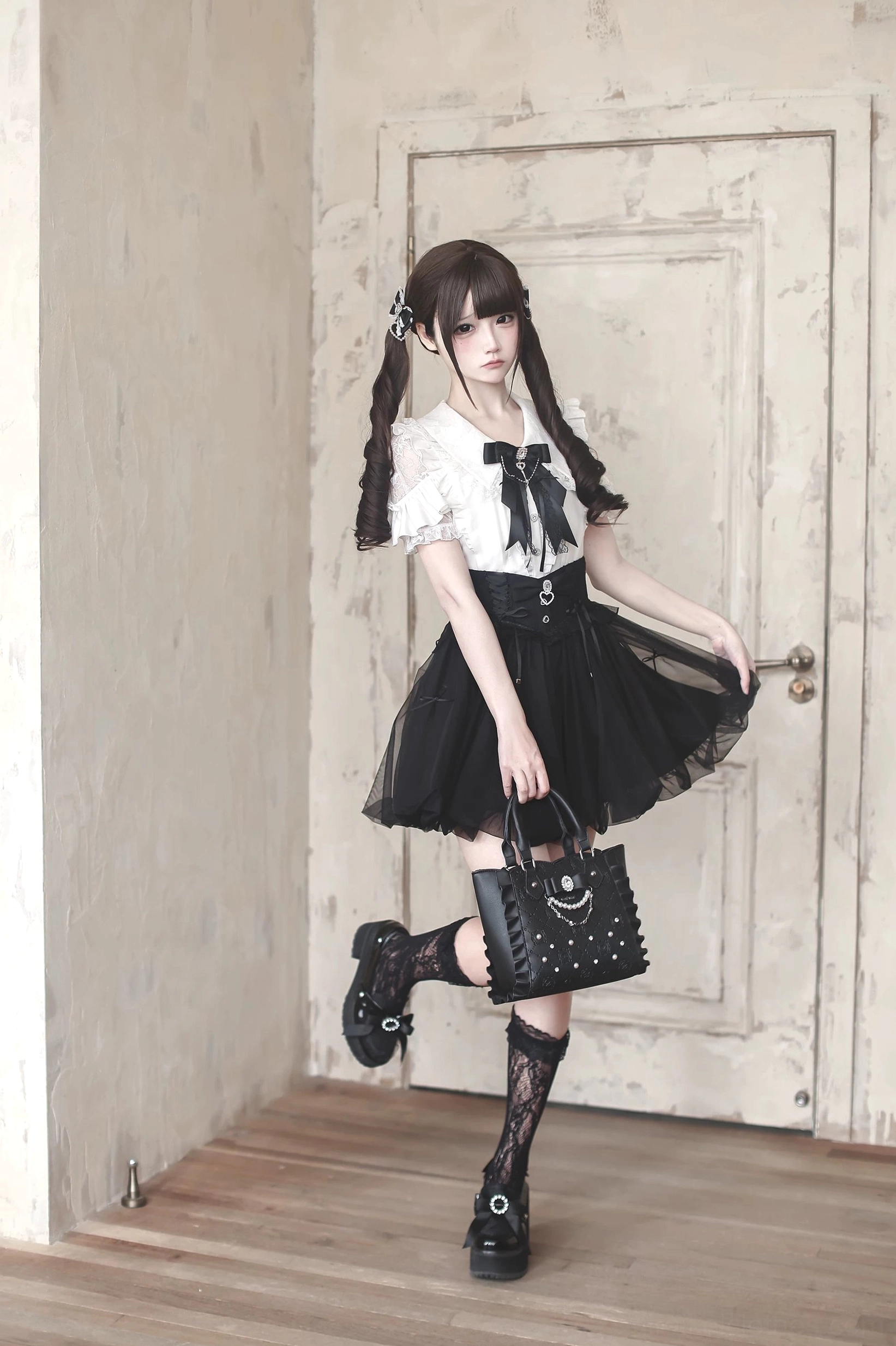 Black and white Jirai Kei two-piece ensemble with bubble skirt, ruffled blouse, tulle layers and platform lace-up shoes, full body model shot against door