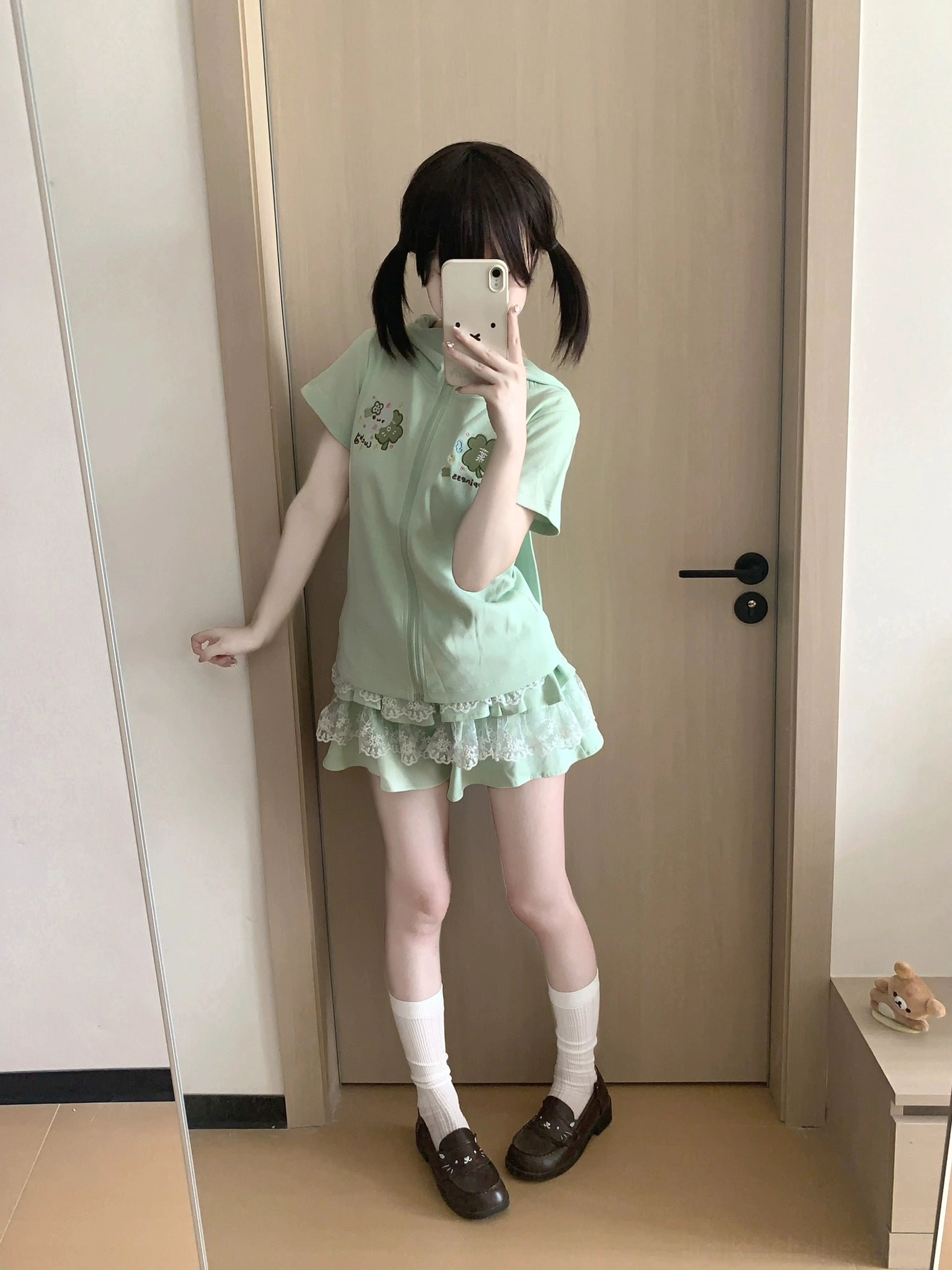 Mint green two-piece Jirai Kei outfit on model with one hand on wall, complete matching short-sleeve hoodie with bunny ear hood and tiered lace ruffle skirt