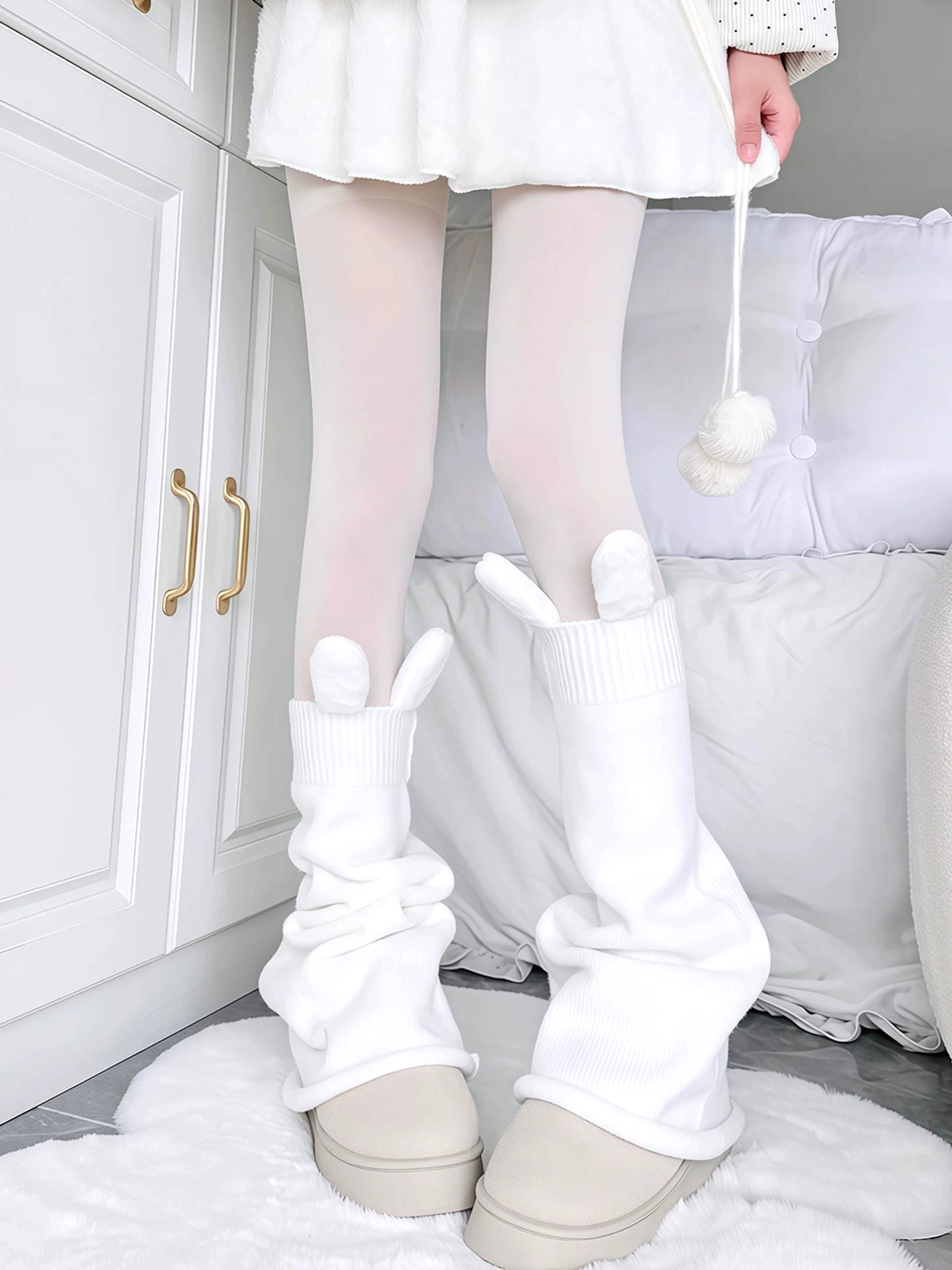 White bunny ear slouchy leg warmers with knitted texture paired with white opaque tights on female model wearing beige platform shoes in minimalist bedroom setting Jirai Kei aesthetic
