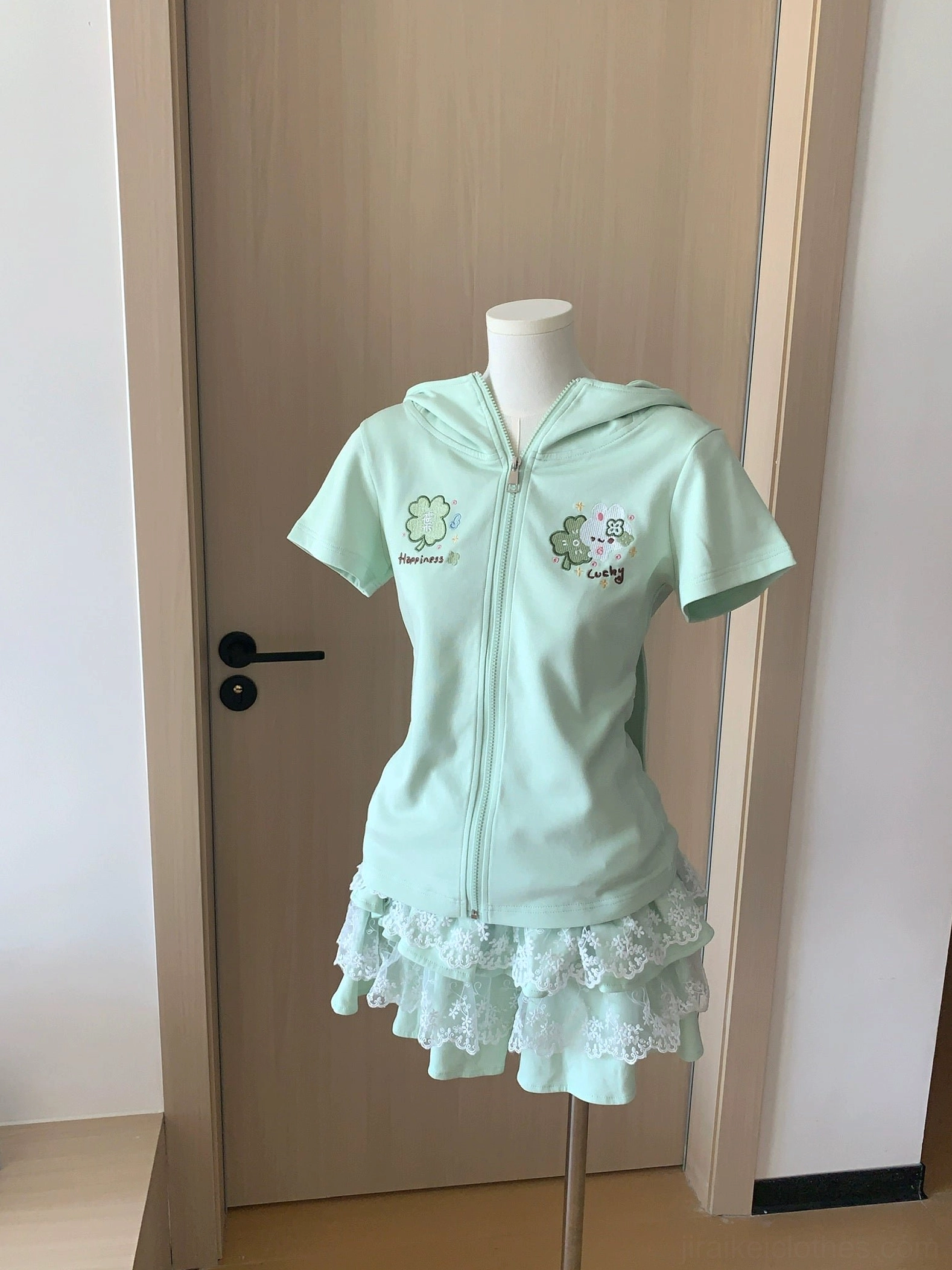 Front flat display perspective of mint green two-piece Jirai Kei outfit showing zip closure, clover embroidery patterns on sweatshirt, and lace-trimmed skirt bottom