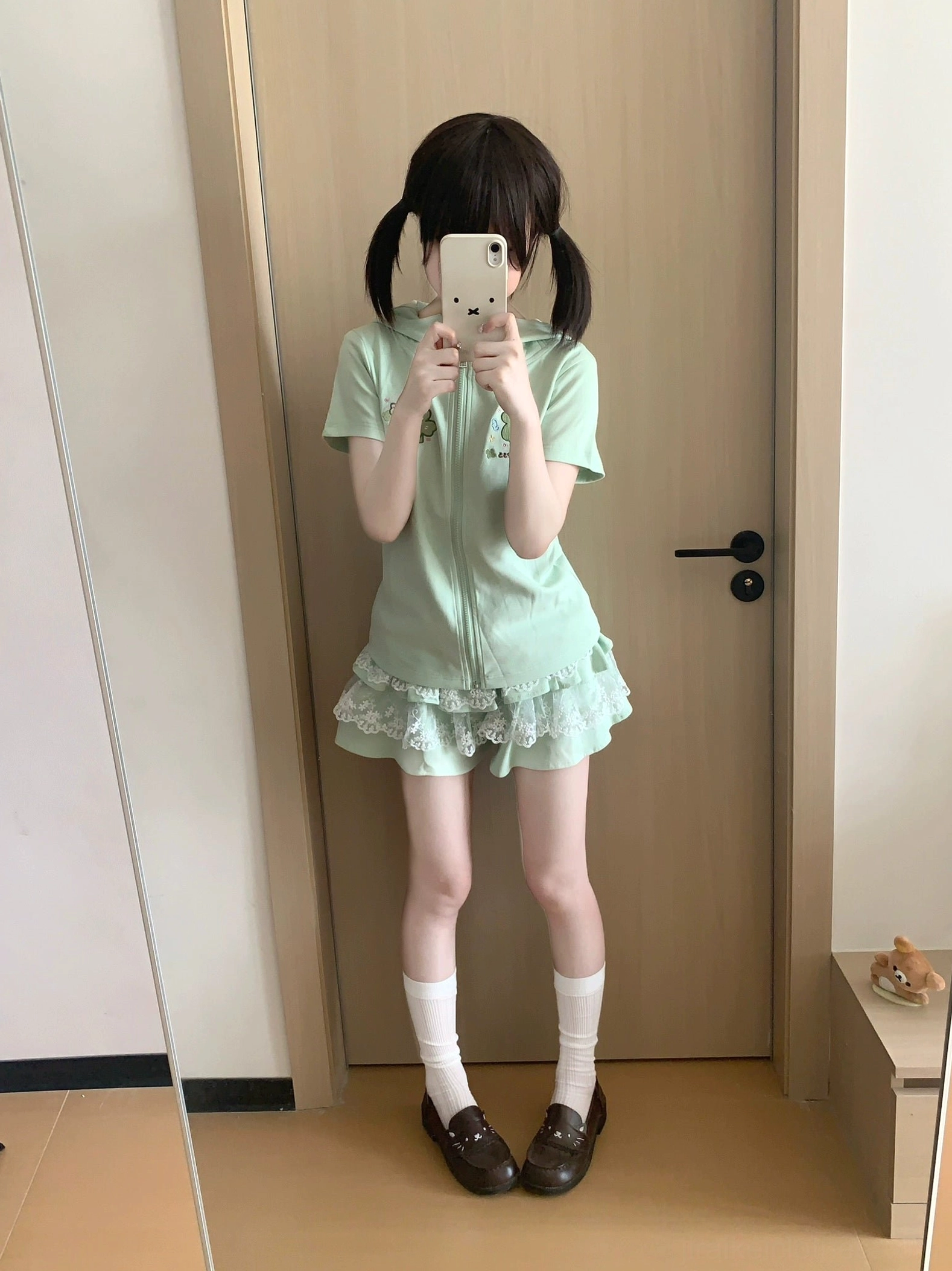 Mint green cute Jirai Kei outfit set on model taking mirror selfie, full view of short-sleeve zip hoodie with bunny ear hood and tiered lace ruffle skirt ensemble