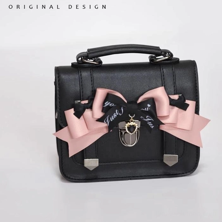 Oblique front perspective of matte black Jirai Kei Cambridge handbag with decorative bow styles and metal lock charms, product detail view
