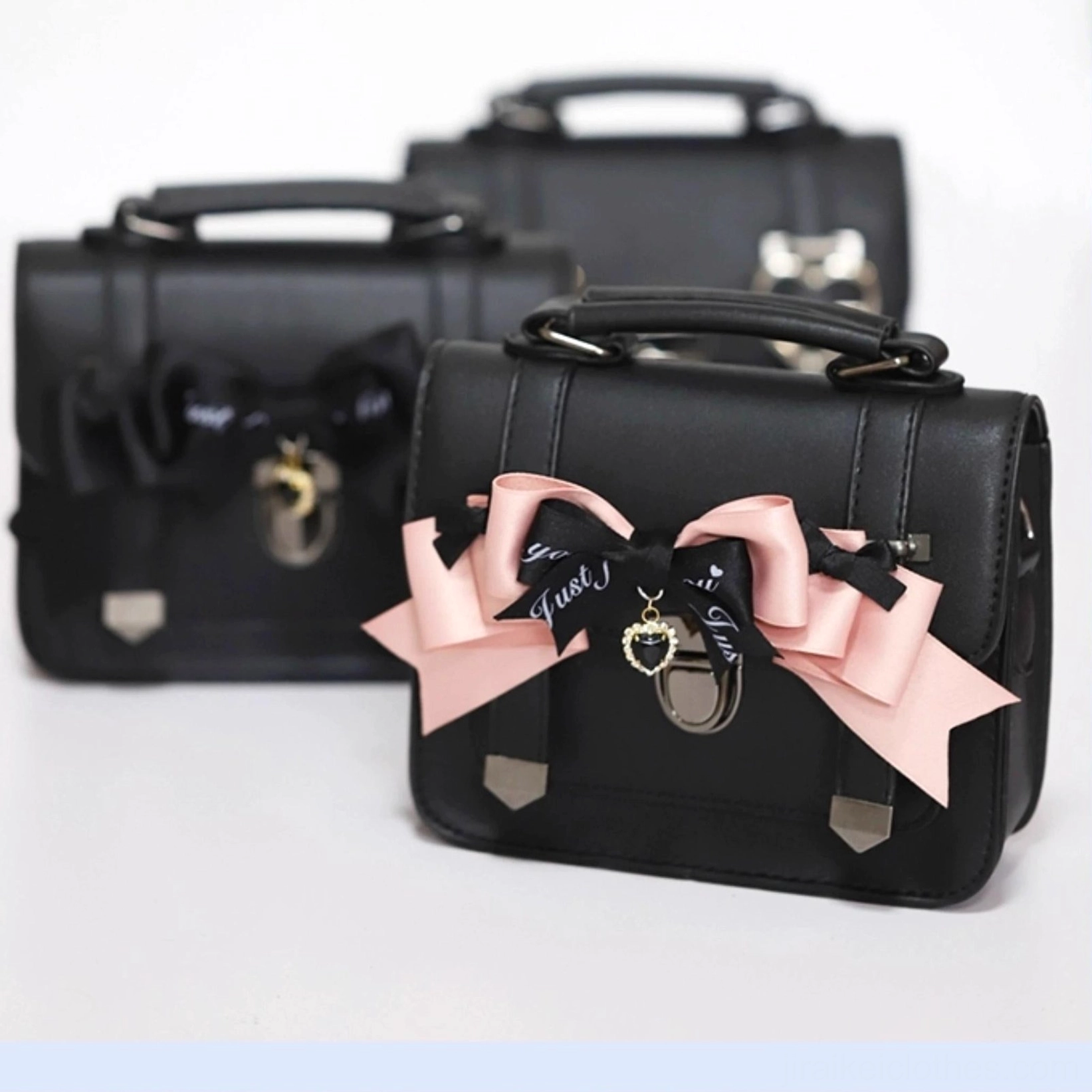 Front oblique angle view of two Jirai Kei Cambridge handbags showcasing pink bow and black bow style variations with matte black PU leather and metal hardware