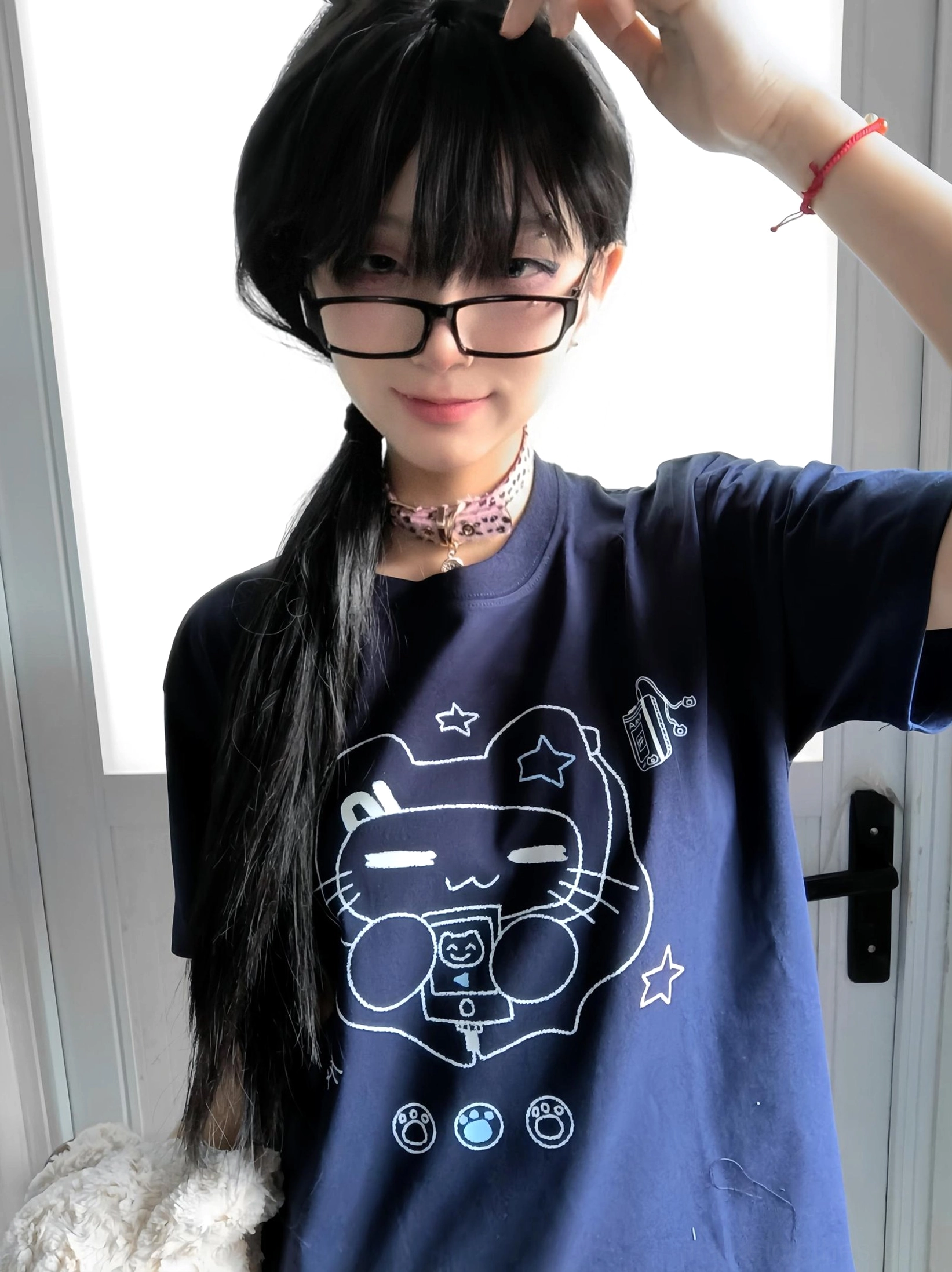Close-up front shot of model wearing navy Jirai Kei cat headset graphic T-shirt with pink choker and eyeglasses indoors