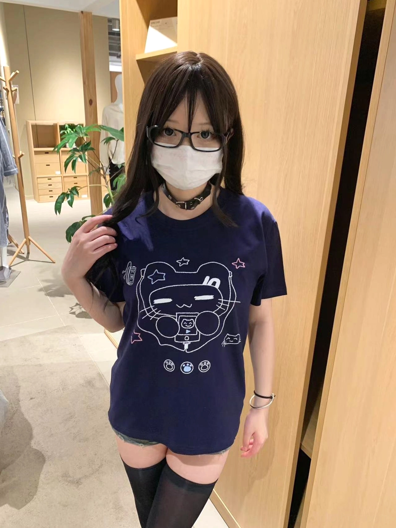 Model wearing navy Jirai Kei cat headset graphic T-shirt styled with thigh-high socks and eyeglasses in indoor clothing store setting