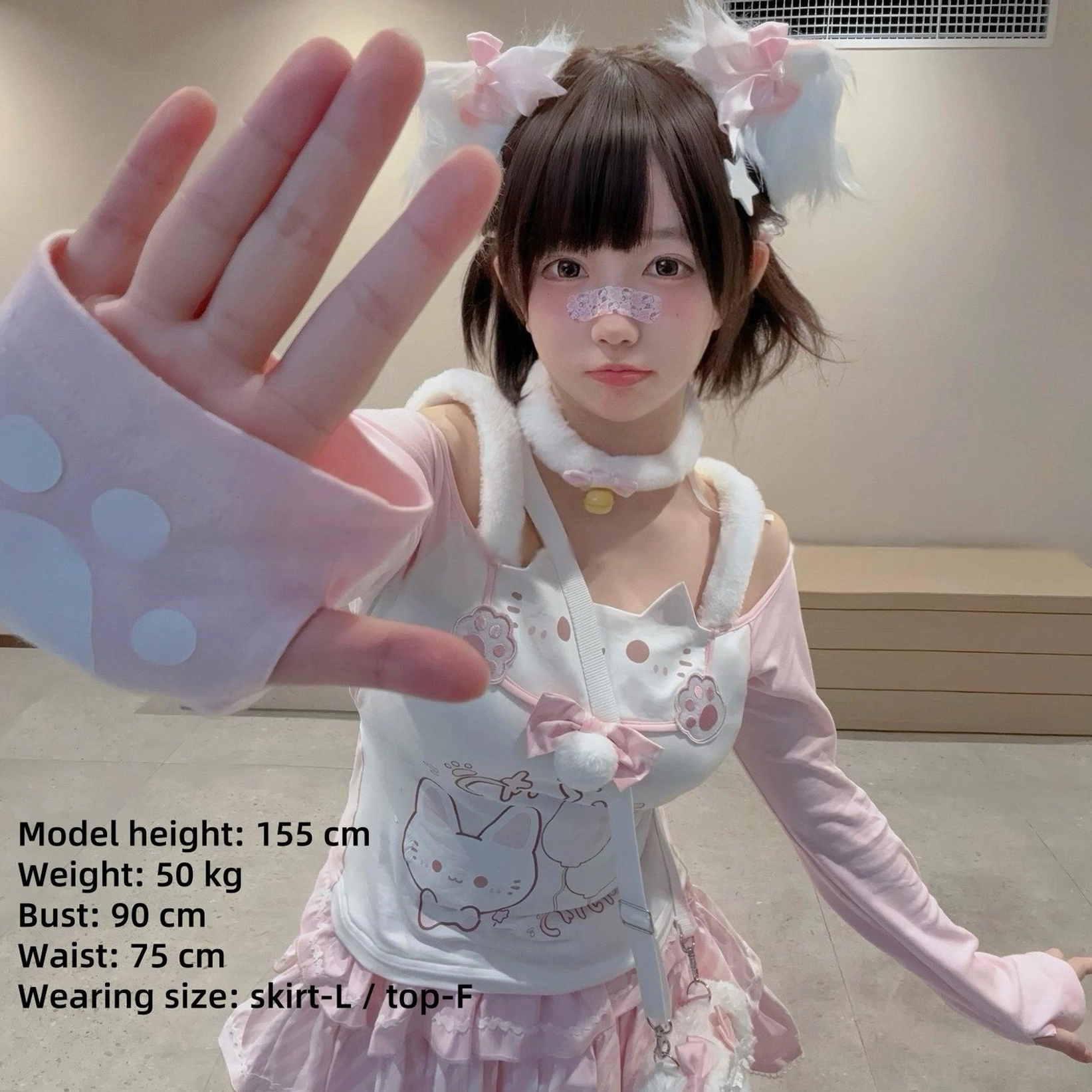 Close-up front selfie shot of model wearing jirai-kei cat-print off-shoulder top with white fuzzy choker and paw-print fingerless gloves, showcasing facial makeup and complete adorable styling