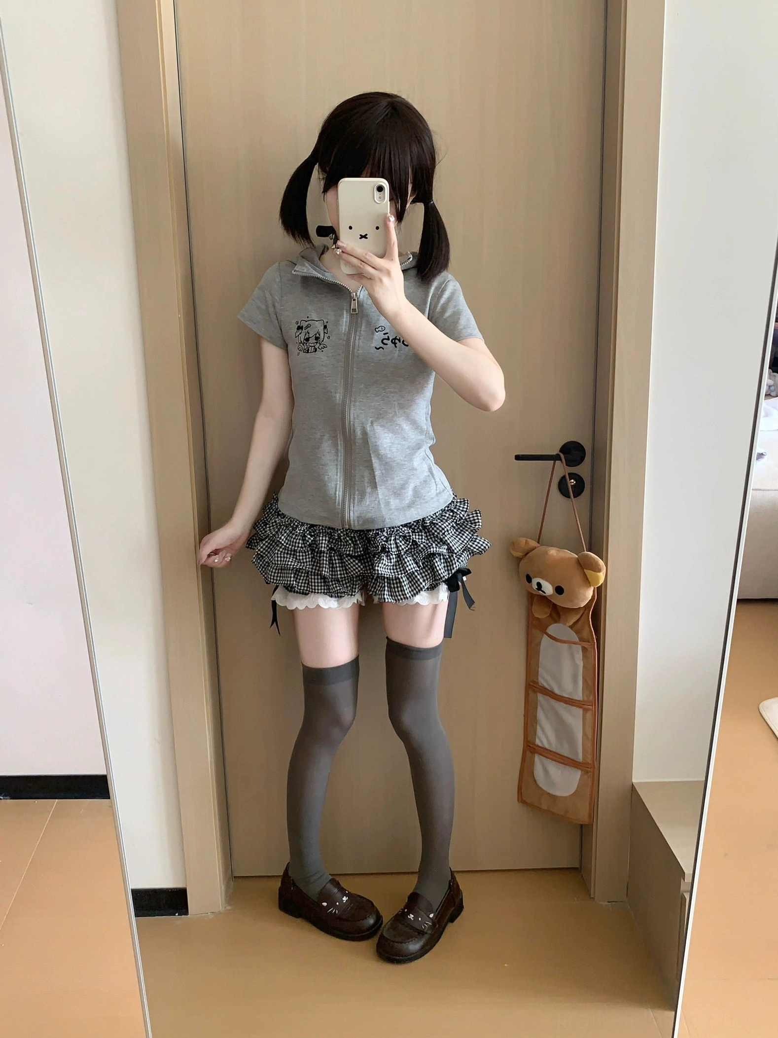 Full-length Jirai Kei daily outfit mirror photo showing relaxed pose wearing black white plaid skirt with bow details grey cropped zip top matching footwear and accessories complete street style aesthetic